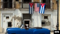 Un automóvil antiguo pasa junto a una casa que exhibe las banderas de Estados Unidos y Cuba en una calle de La Habana (Cuba).
