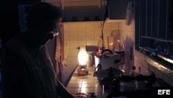 Una mujer lava los platos iluminada por una lámpara de queroseno durante un apagón.